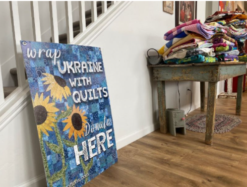 Poster next to stacks of quilts for Ukraine