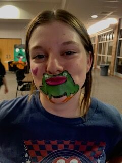 Girl pursing her lips to create the mouth of the frog in her face paint.