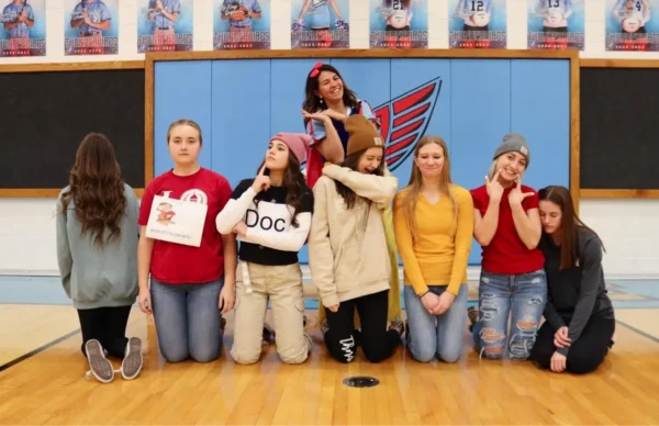 Snow White stands behind seven girls posing as the seven dwarfs (grumpy face, sneezing, etc.)