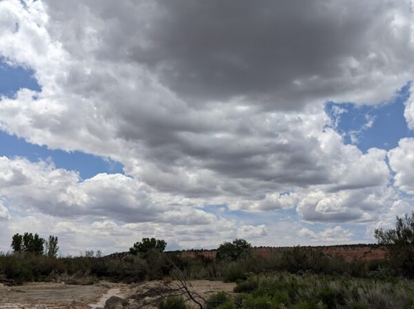 A somewhat dark sheet of clouds over a red rock mountain.