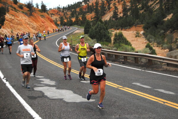 Runners run down a hilly road near red rocks in the bryce canyon half marathon