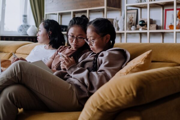 A group of young girls sits on a couch looking at a phone.