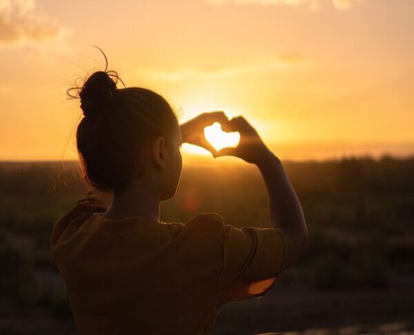 Girl making a heart over the sunset.