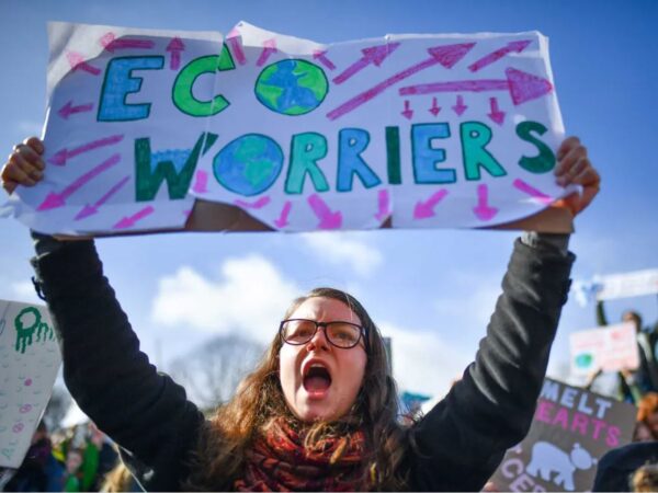 A teenage girl holds up a sign reading, "Eco Worriers," and indicating her generation.