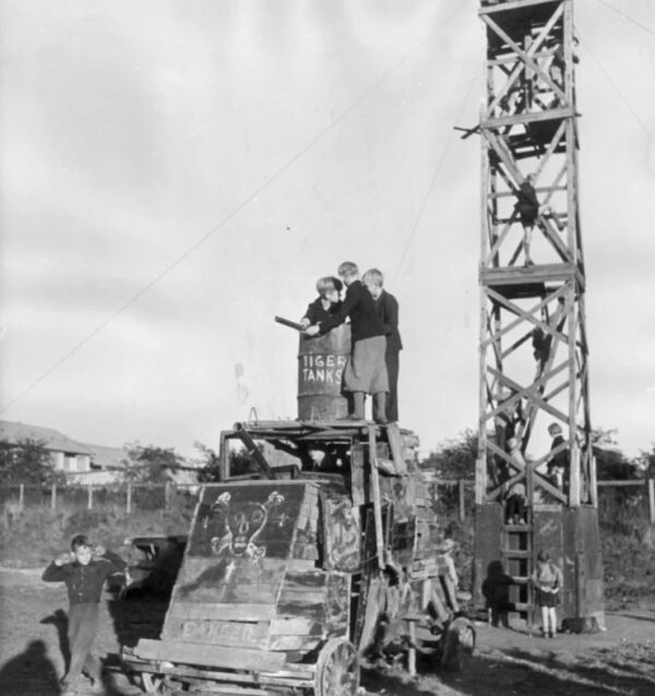 A black a white picture shows young children playing in what looks like a huge junkyard.