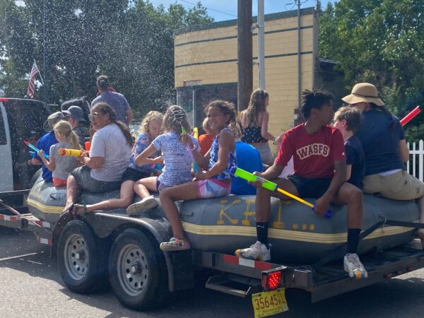 A group of kids rides on a raft float spraying spectators with water guns.