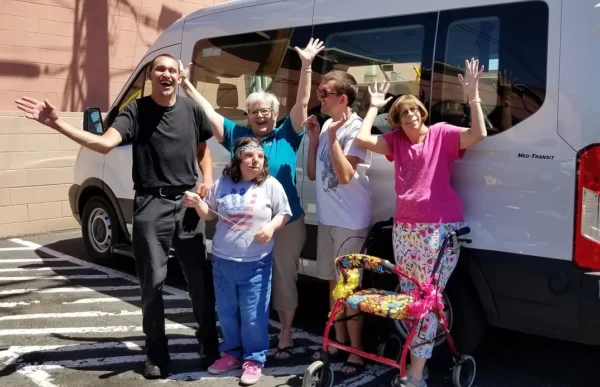 A group of people with disabilities raises their hands to celebrate a new van.