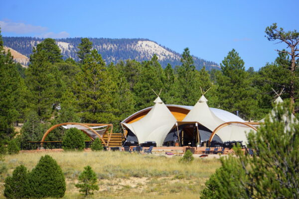 A canvas TP on a glamping site near red rocks, desert grasses, and evergreen trees.
