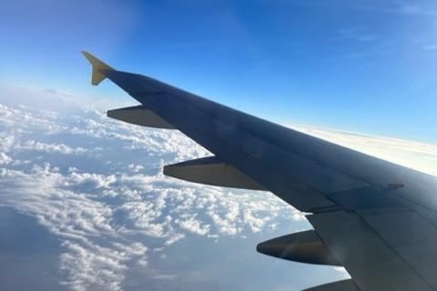 The view of a plane's wing outside its window as it flies above the clouds.