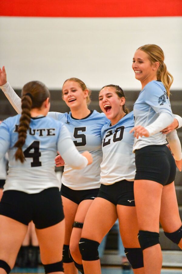 Five volleyball players jump and celebrate on the court.