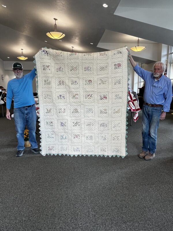Two men hold up a large white quilt.