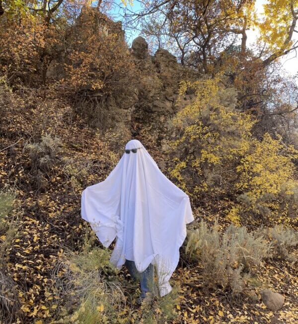 A person dressed as a cool ghost in sunglasses poses with the fall mountain leaves.