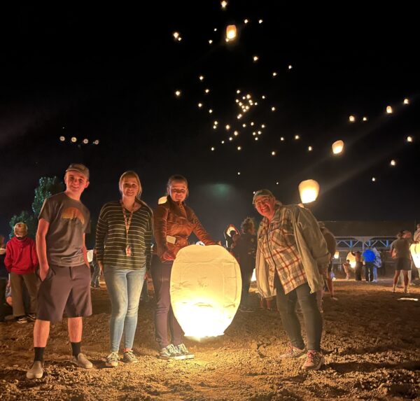 A sky full of lanterns shows behind the group as they prepare to send off the last one.