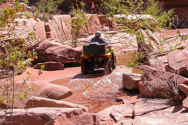 An person on an all-terrain vehicl (ATV) driving through a rocky river wash.