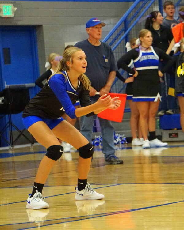 A Panguitch volleyball player crouches low, preparing to bump the ball.