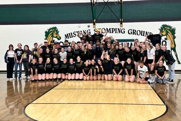 A huge group of volleyball players, cheerleaders and fans poses, all dressed in black and gold.