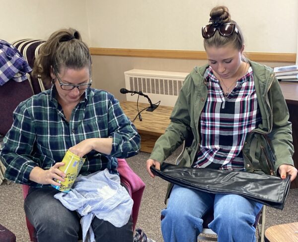 Two women lay out clothing on their laps as they prepare to pin and hem them.
