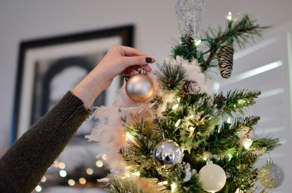 A hand reaching to the top of a Christmas tree to place an ornament.