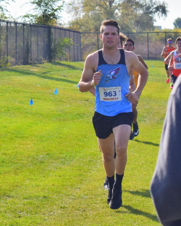 A Piute boys cross country runner runs on a stretch of green grass at a park.