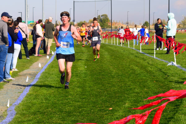 A Piute boys cross country runner sprints into the flagged finish line chute, with an Escalante boy not far behind.