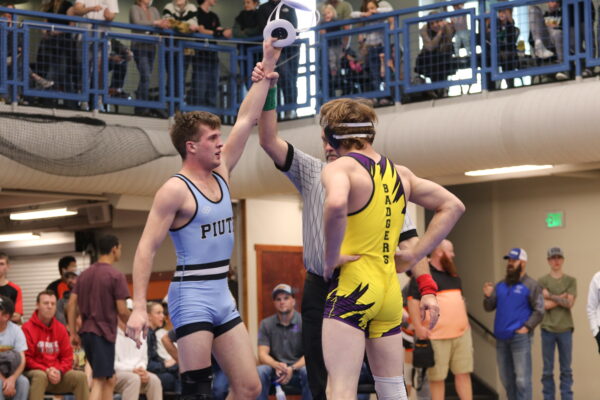 The referee holds up a Piute wrester's hand to indicate the winner of the match.