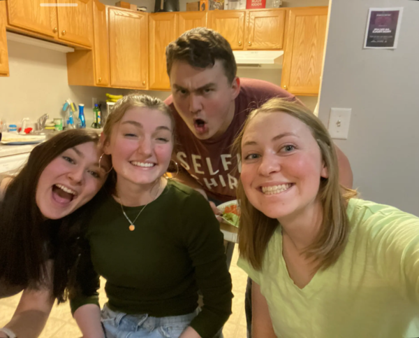 Four college students pose for a picture in an apartment kitchen.