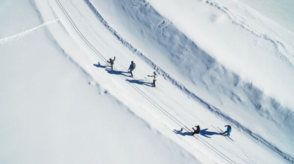 An aerial shot of a group of five cross country skiing on a packed track of snow.