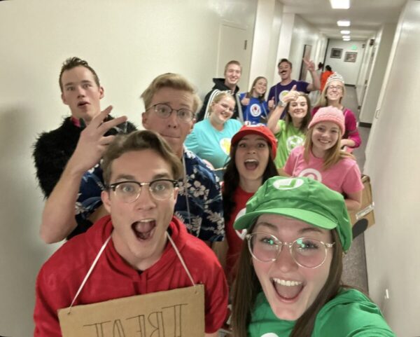 A large group of college students in a dorm hallway dressed like characters from a Mario video game.