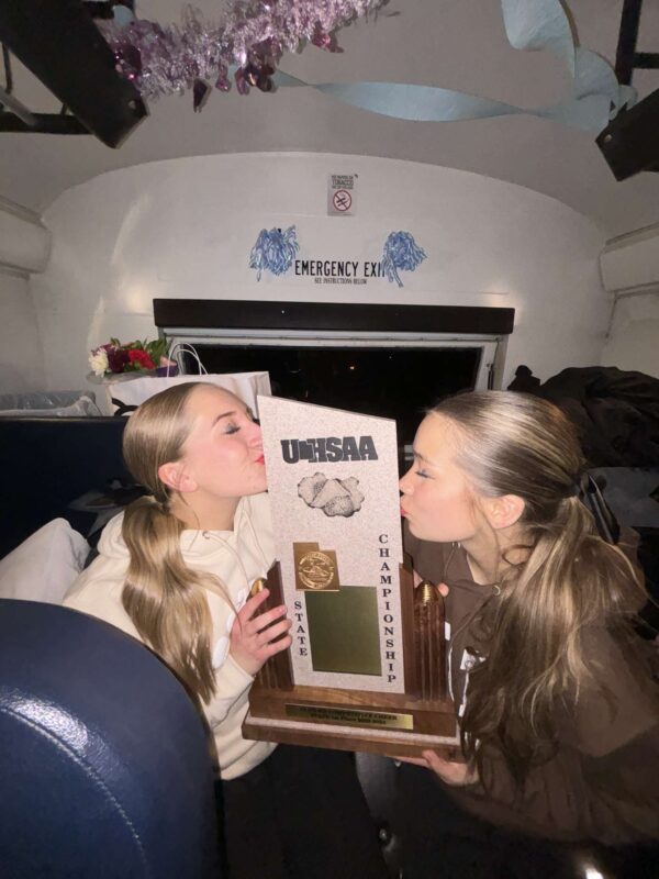 Two Piute cheerleaders kiss their 2024 state championship trophy.
