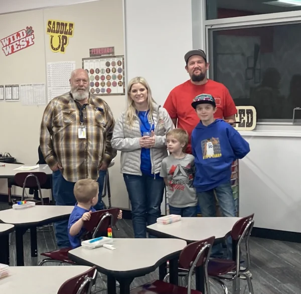 A family poses in a classroom with their elementary school teacher.