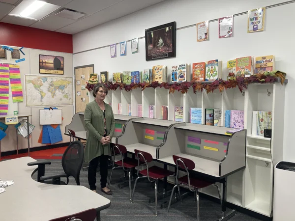 A woman stands in an Escalante Elementary School classroom by shelves with a number of carefully-displayed hand drawn book covers.