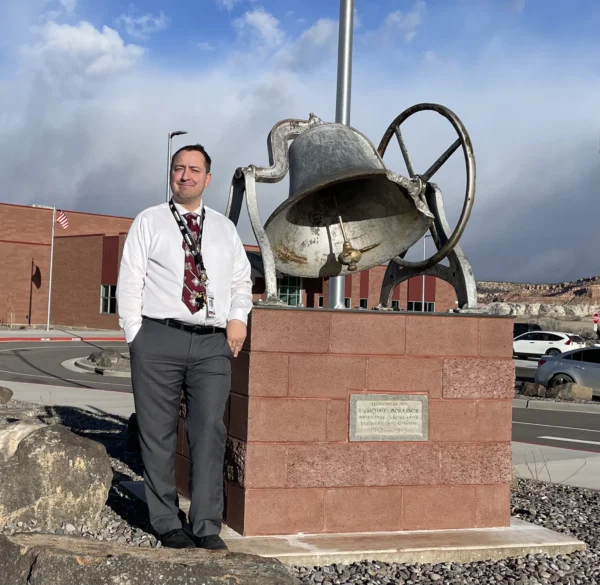 Escalante's principal stands by the old school bell outside of Escalante's new elementary school.