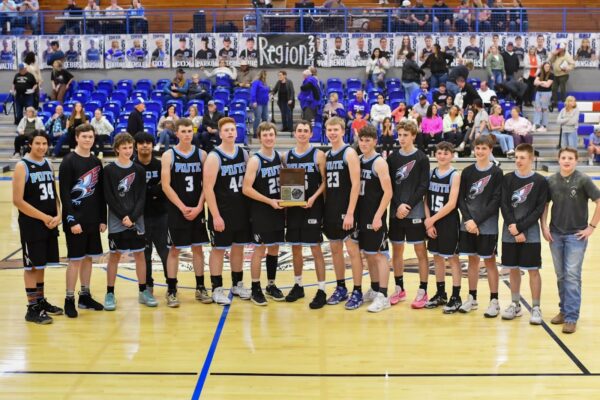 The Piute boys basketball team takes a group photo on the court with the region trophy.