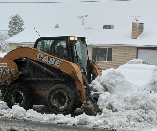 A man shovels piles of fluffy, white snow in a skid steer.