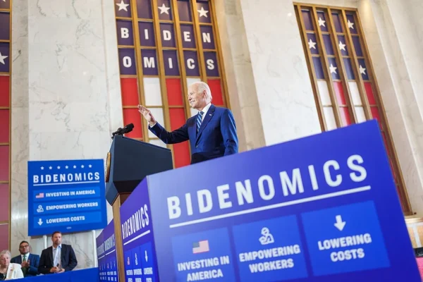 Joe Biden speaks from a pulpit surrounded by blue "Bidenomics" signs.