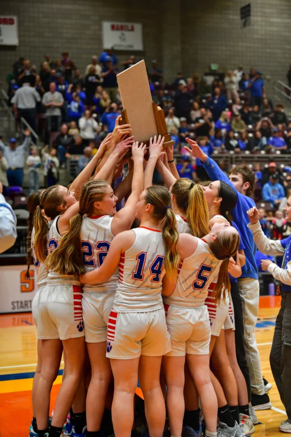 The Panguitch girls basketball team stands in a huddle holding up their 1A state basketball trophy.