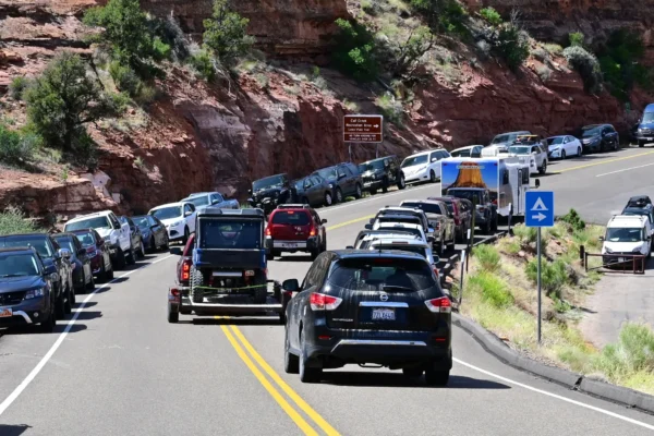 Drivers go around parked cars on both sides of the road near the red rocks and desert area of Calf Creek.