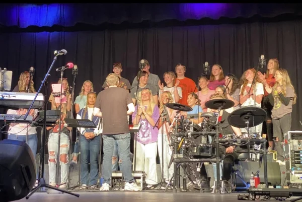 Piute choir, wearing ripped jeans and shirts with the logos of rock and roll bands on them, claps and smiles at their rock concert under the direction of Tyrel Ivie.
