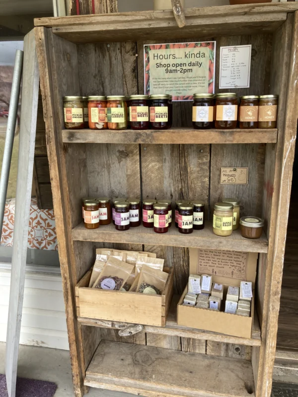 A shelf with jars of jam and homemade signs showing pricing and hours.