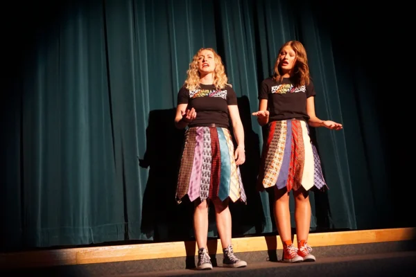 The narrators (Taylor LeFevre and Bradi Gates) sing in front of the curtain.