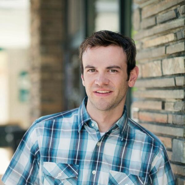 A professional headshot of Tyler Whitesides. He has brown hair and brown eyes and wears a blue, plaid collared shirt.