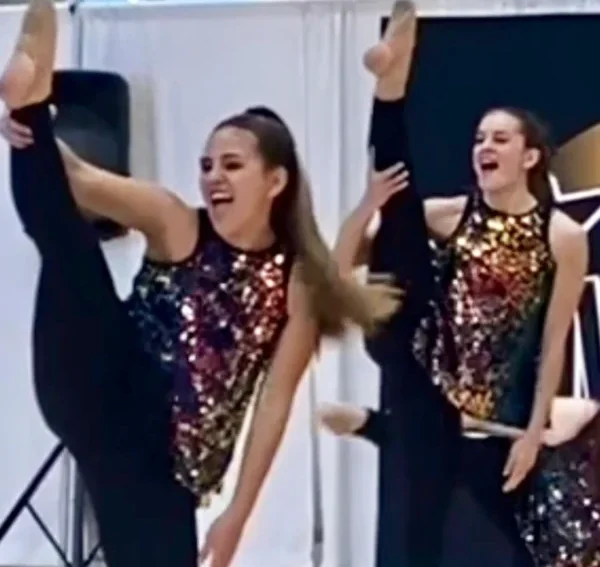 Piute dance company lift their heels in the air for a heel stretch. They wear colorful sequined shirts.