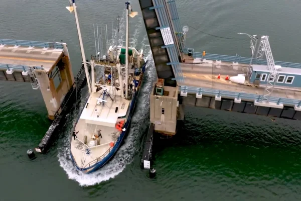 A fishing vessel traveling on the water through a toll bridge.