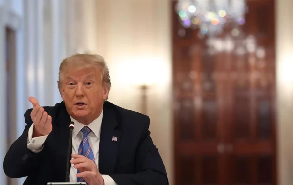 Donald Trump sitting at a stage and speaking in a microphone.