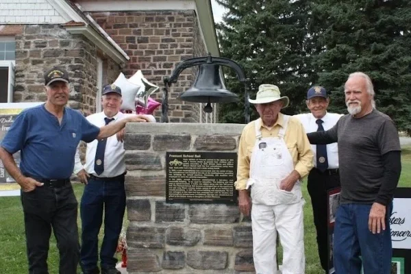 A group of men standing around the Fremont school bell on a monument with a plaque.