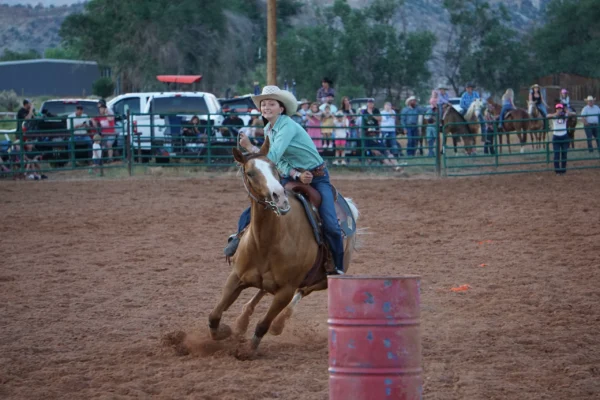 A teenage girl races her horse around a barrel in a rodeo arena.