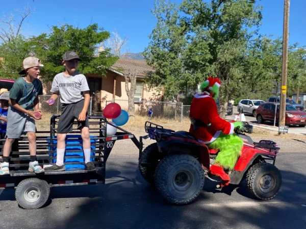 A person dressed as The Grinch drives a four-wheeler while boys on a trailer on the back throw water balloons.