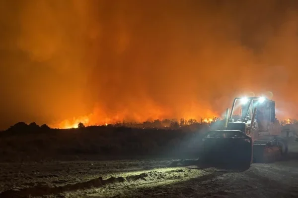 Orange smoke covers the sky at night during the Silver King Fire. A dozer works on a line in the foreground with its headlights on.