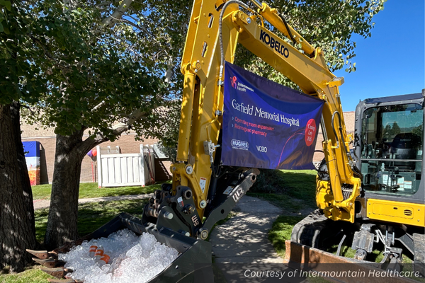 An excavator at the Garfield Memorial Hospital groundbreaking holding drinks and a sign. Courtesy of Intermountain Healthcare.