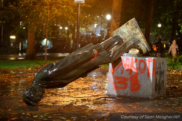 A toppled and graffitied statue of Abraham Lincoln in the city at night. Courtesy of Sean Meagher/AP.